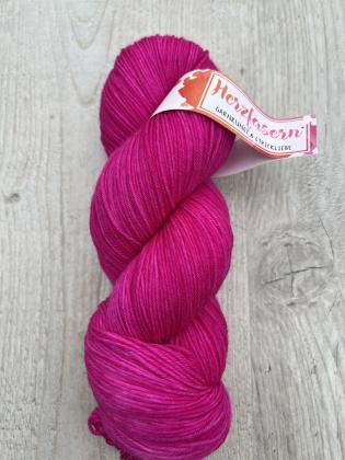 Handgefärbter Wollstrang in kräftigem Pink (Herzfasern 2.0) auf heller Holzoberfläche. Das Garn ist gleichmäßig gefärbt und zeigt eine glatte, feine Struktur. Banderole mit dem Schriftzug „Herzfasern – Garnkunst & Strickliebe“.